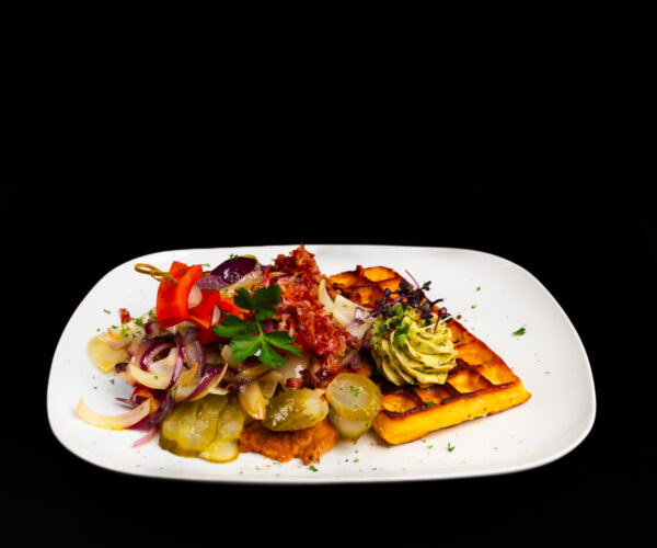 „Bautz‘ner Senfsteak“ Schweinekammsteak in Senf-Ei-Hülle gebraten, an herzhafter Kartoffelwaffel, garniert mit Speck, brauner Zwiebel und saurer Gurke, dazu Kräuterbutter