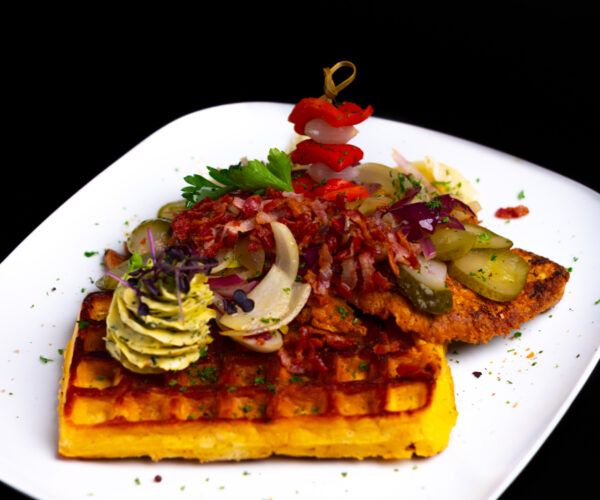 „Bautz‘ner Senfsteak“ Schweinekammsteak in Senf-Ei-Hülle gebraten, an herzhafter Kartoffelwaffel, garniert mit Speck, brauner Zwiebel und saurer Gurke, dazu Kräuterbutter